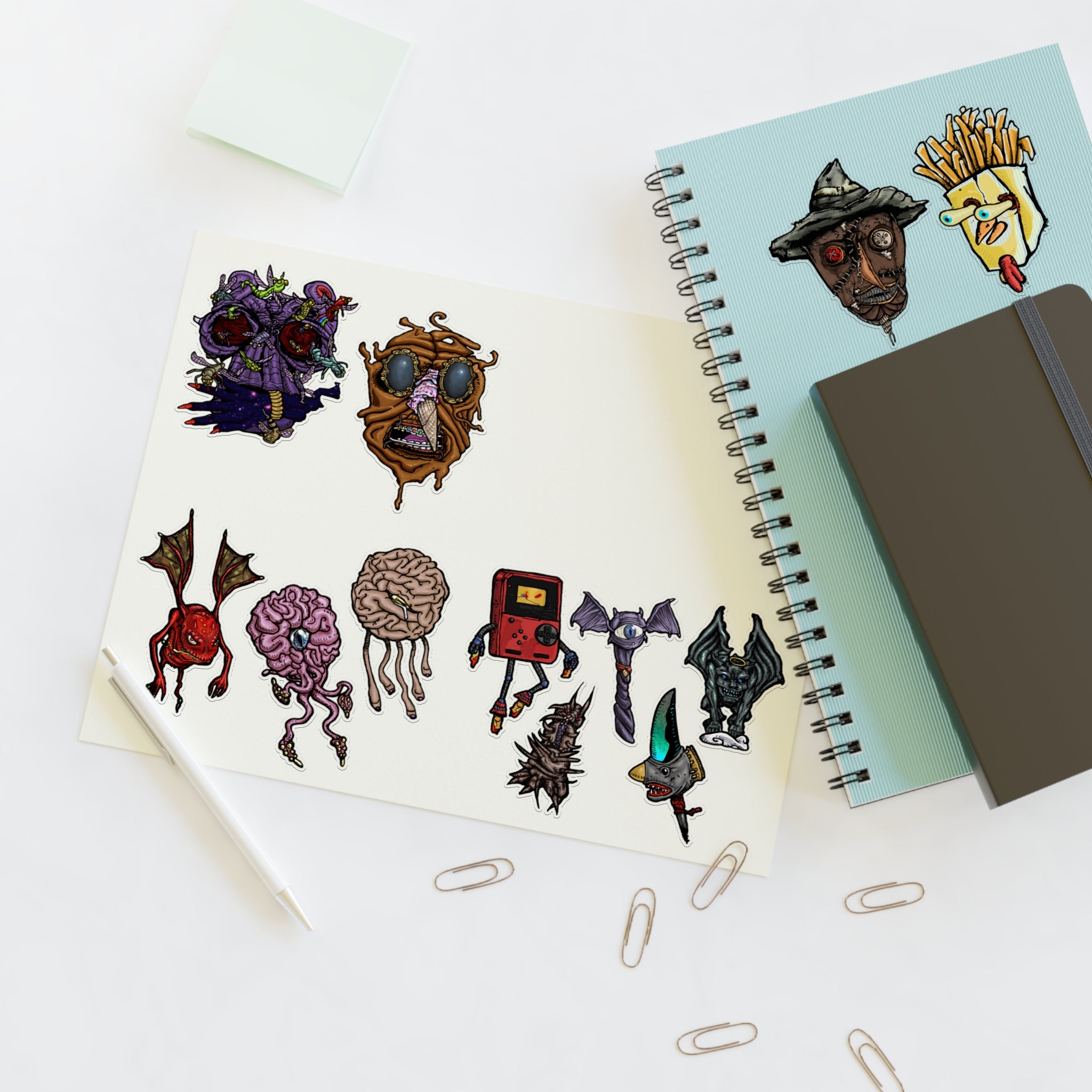 Freaky Features Sticker Sheet Set #3 , transparent die-cut sheet with 12 hand-drawn monsters and creatures including alien swarm, melting chocolate head, scarecrow, french fry box, walking Game Boy ( Gamerpal) , brains, and various weird weapons/creatures
