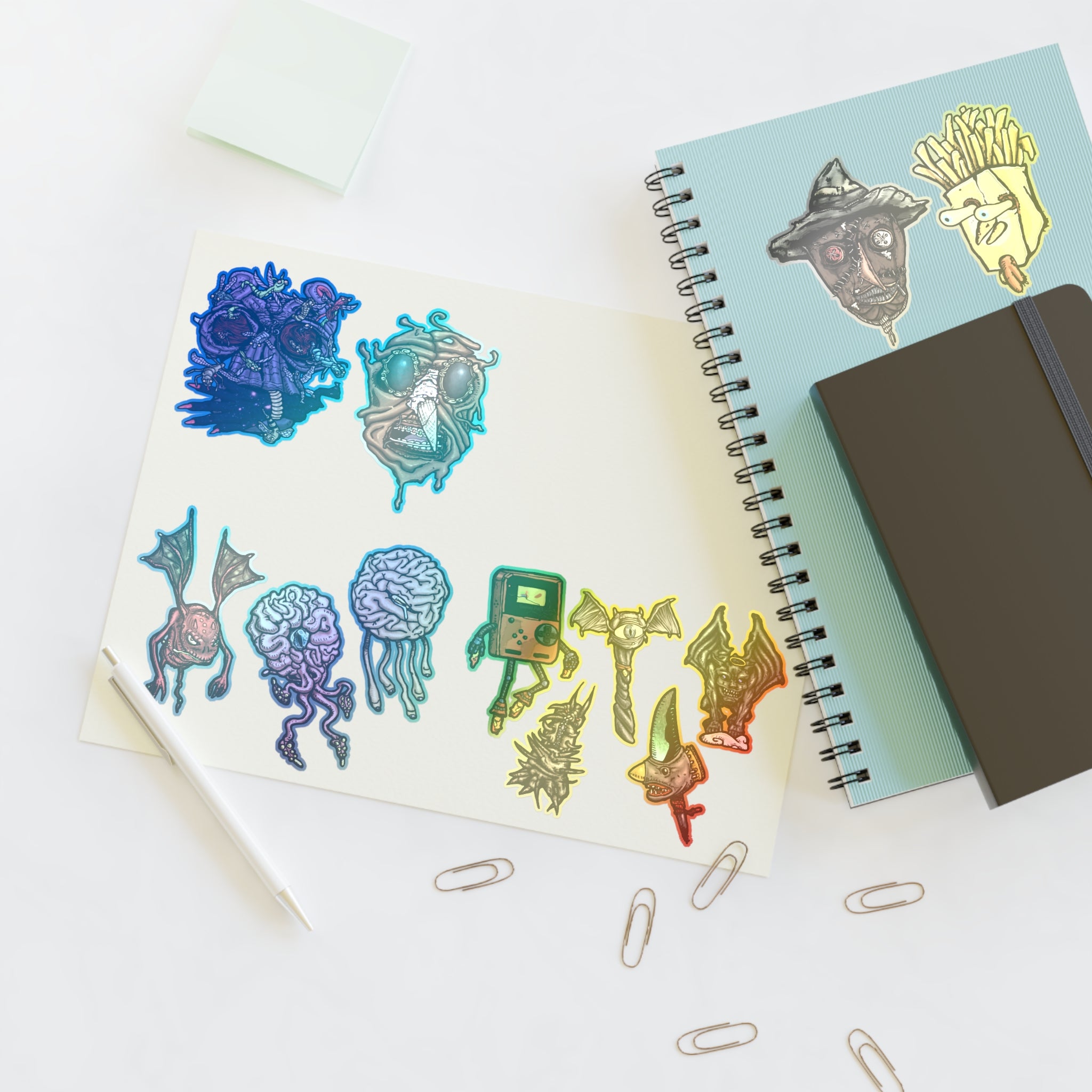 Freaky Features Sticker Sheet Set #3 , transparent die-cut sheet with 12 hand-drawn monsters and creatures including alien swarm, melting chocolate head, scarecrow, french fry box, walking Game Boy ( Gamerpal) , brains, and various weird weapons/creatures
