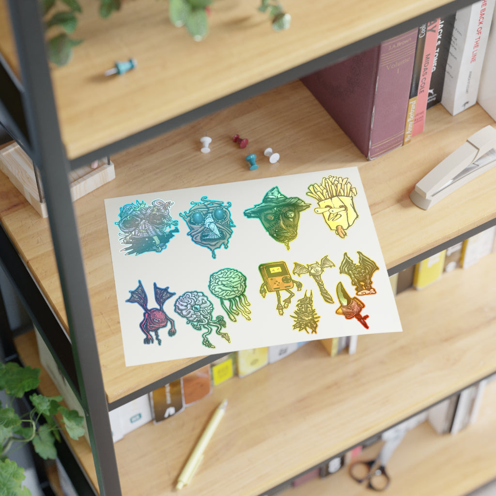 Freaky Features Sticker Sheet Set #3 , transparent die-cut sheet with 12 hand-drawn monsters and creatures including alien swarm, melting chocolate head, scarecrow, french fry box, walking Game Boy ( Gamerpal) , brains, and various weird weapons/creatures
